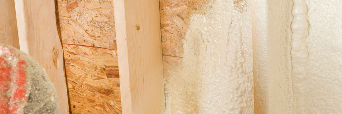 Construction worker spraying expandable foam insulation between wall studs