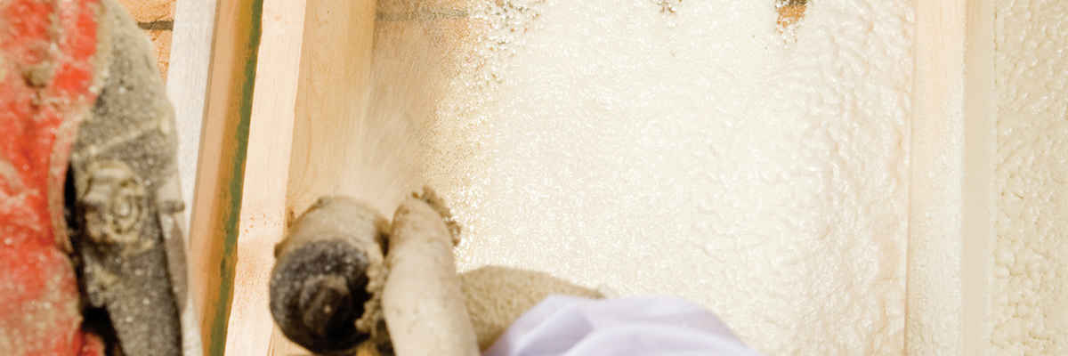 Construction worker spraying expandable foam insulation between wall studs