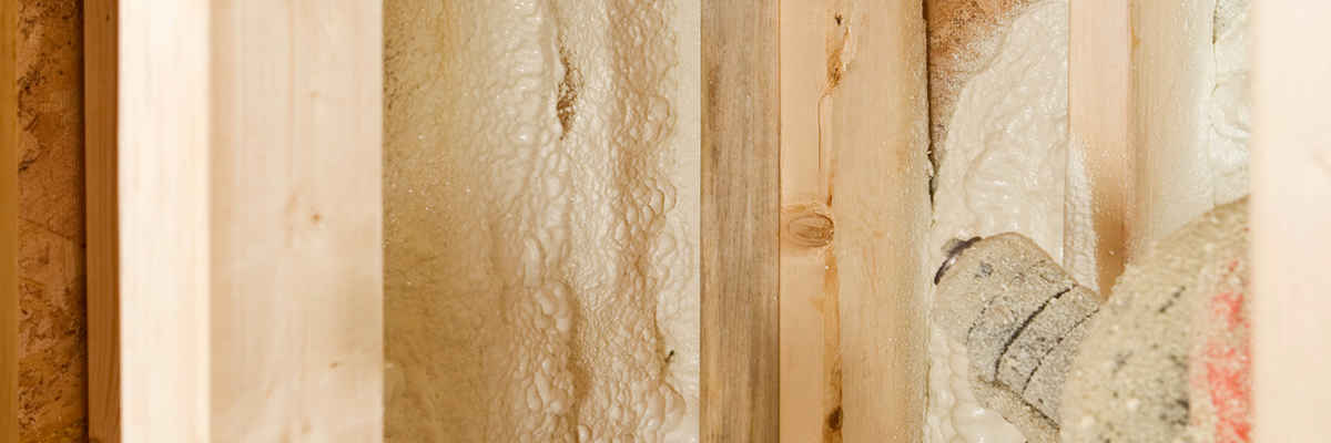 Construction worker spraying expandable foam insulation between wall studs